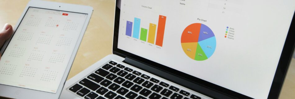 A laptop displaying bar and pie charts with a calendar on a tablet next to it.