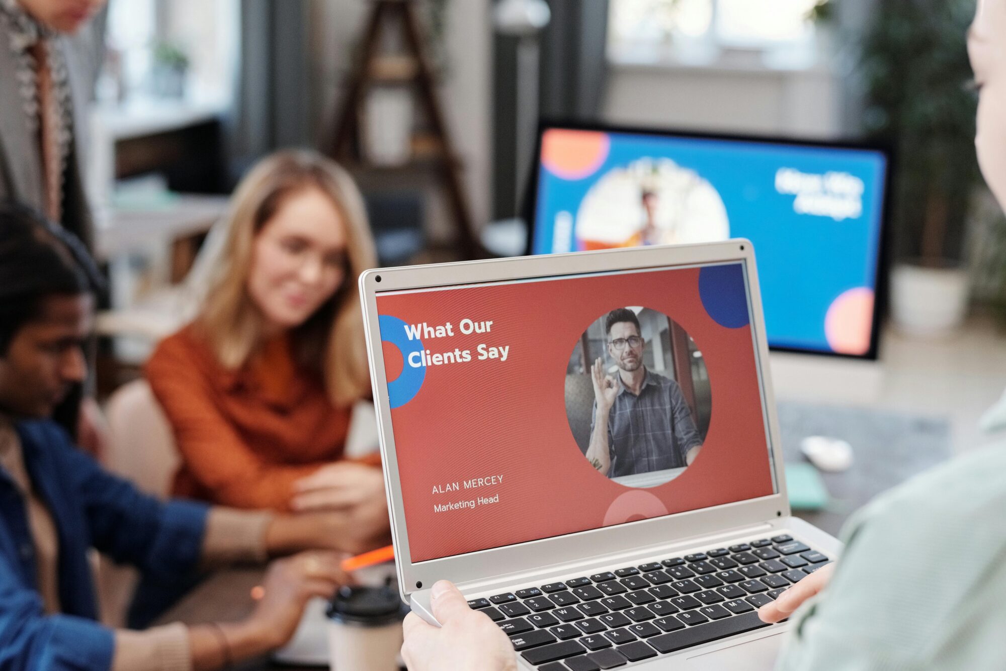 A team reviewing client feedback on a laptop screen, with a presentation titled "What Our Clients Say" showing a satisfied customer.