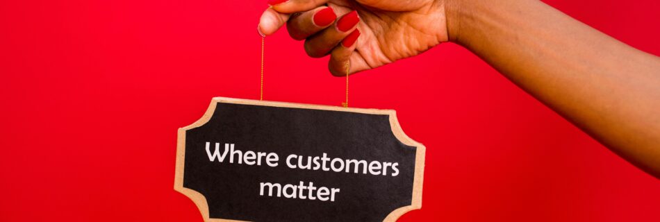 A hand with red-painted nails holding a black sign that says "Where customers matter" on a red background, symbolizing the value of prioritizing customers.