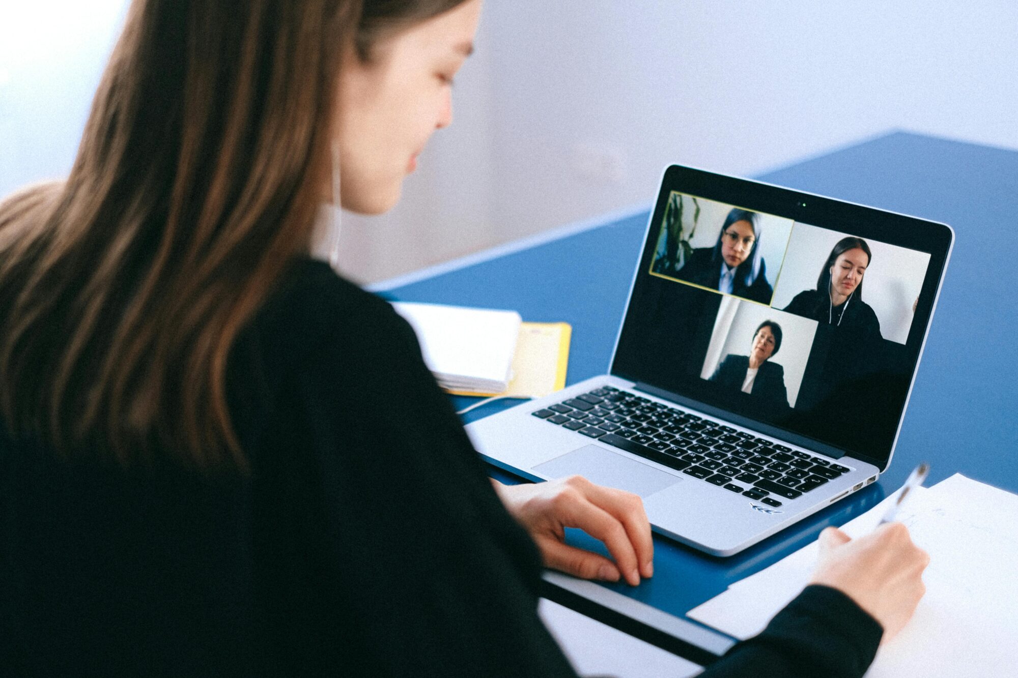 A woman is participating in a virtual meeting on her laptop, displaying four people on the screen.