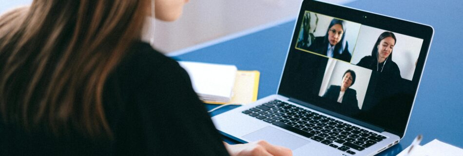 A woman is participating in a virtual meeting on her laptop, displaying four people on the screen.