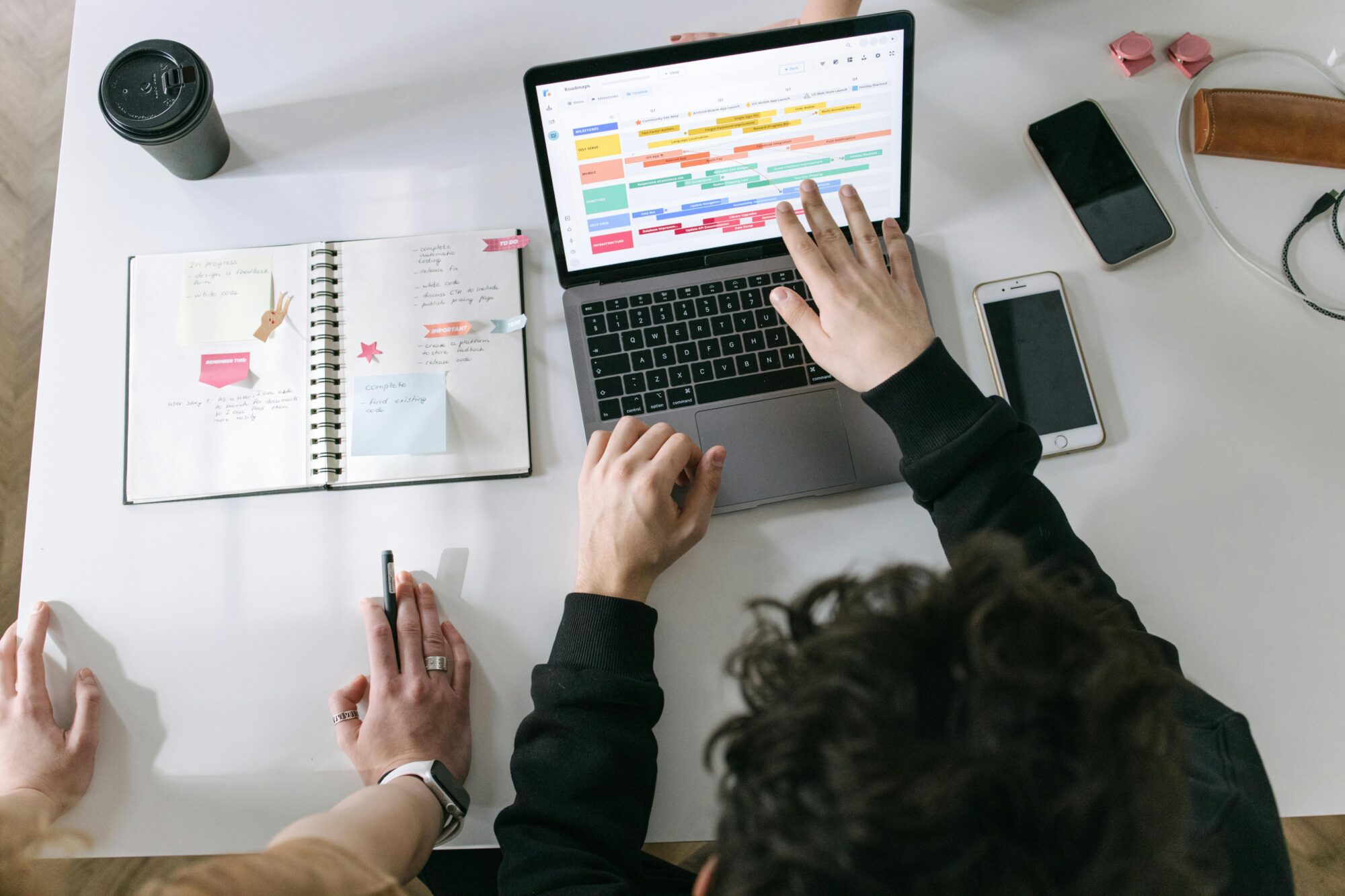 Two individuals collaborating on a project, using a laptop with a task scheduler and an open notebook for planning