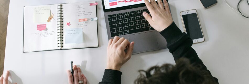 Two individuals collaborating on a project, using a laptop with a task scheduler and an open notebook for planning