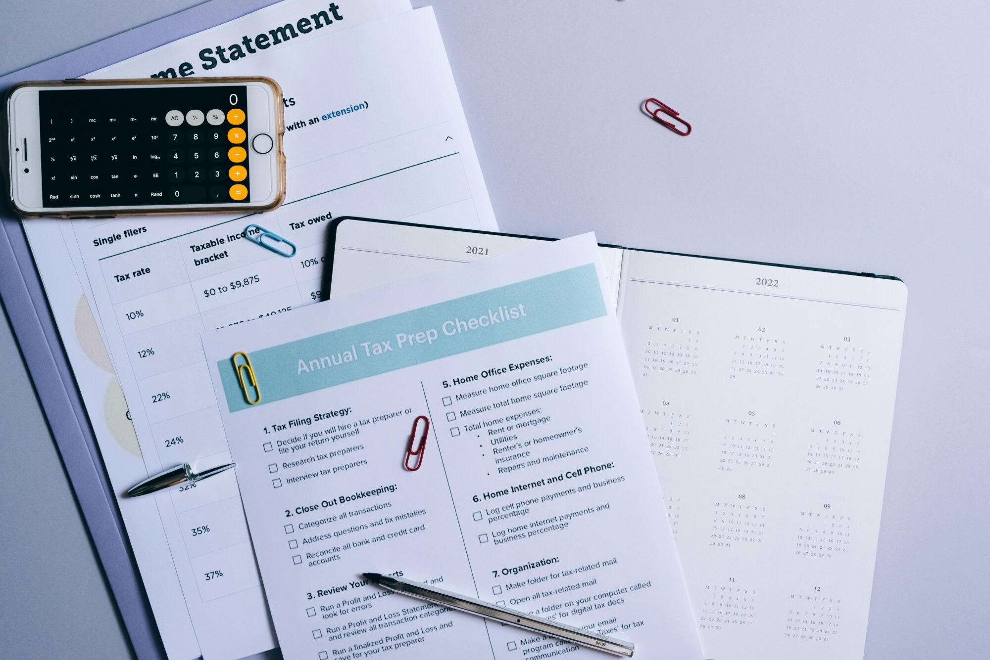 A tax preparation checklist, financial documents, a calculator, and a planner laid out on a desk for annual tax filing.