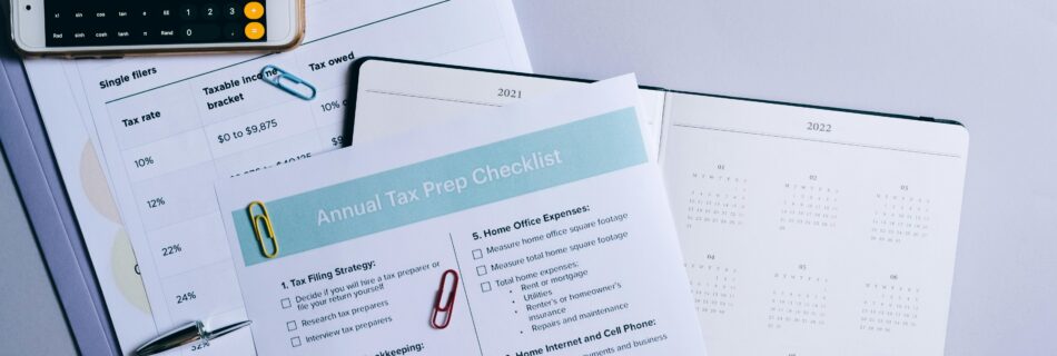 A tax preparation checklist, financial documents, a calculator, and a planner laid out on a desk for annual tax filing.