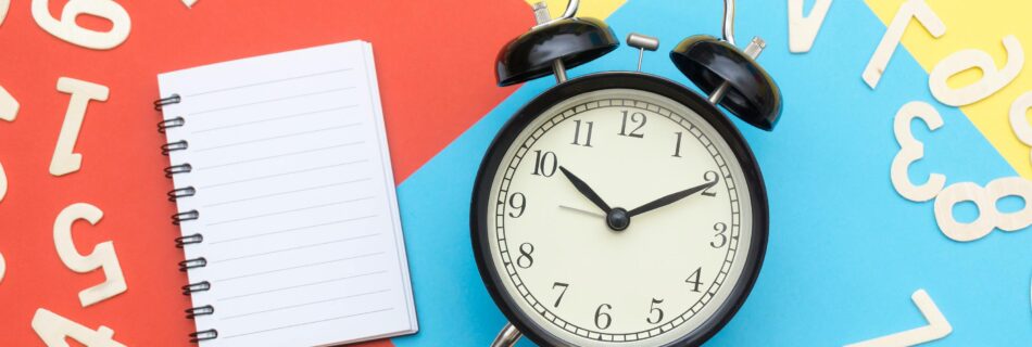 Alarm clock with a blank notebook and scattered numbers on colorful background, symbolizing time management and planning