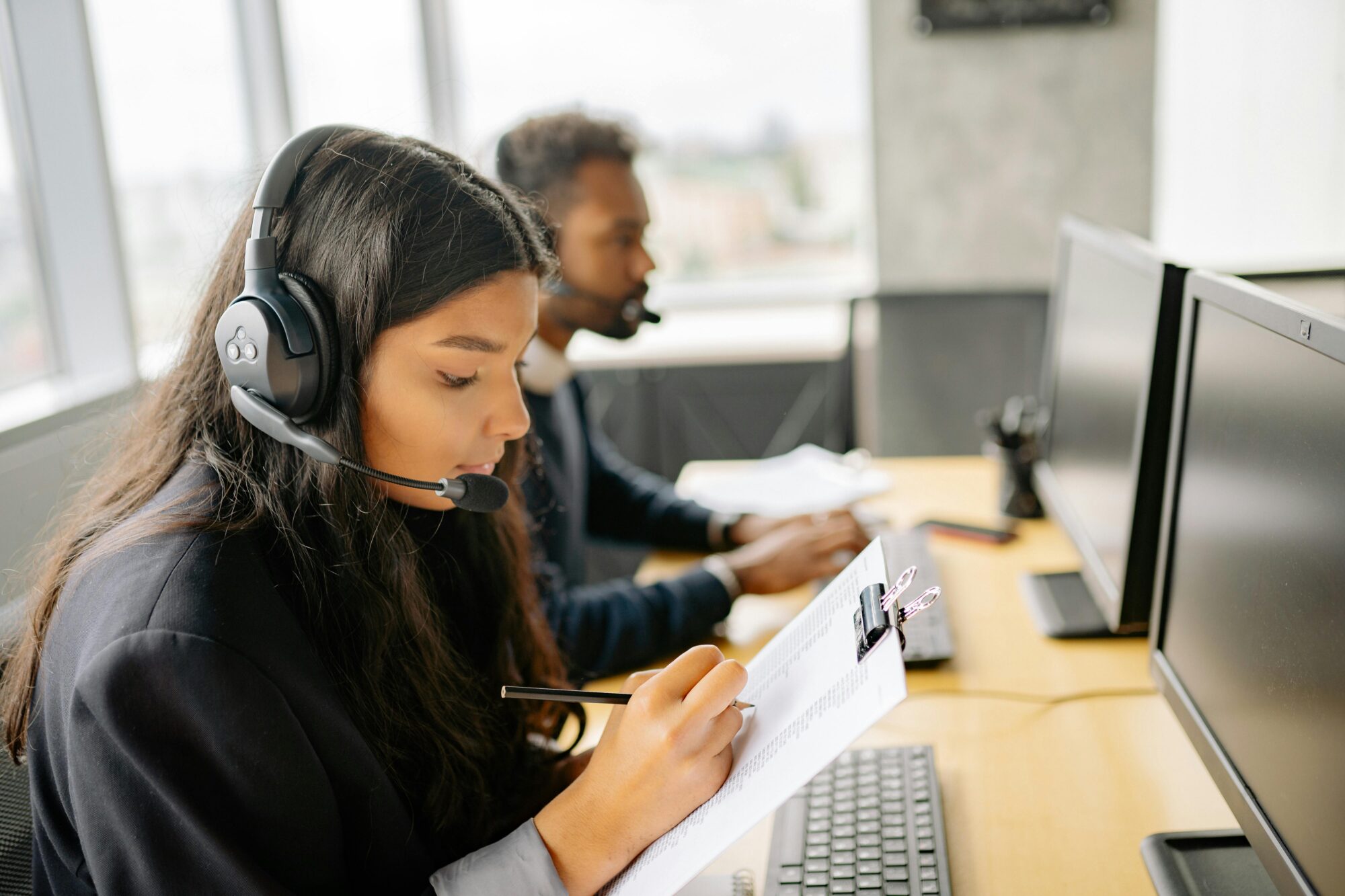 Virtual assistants wearing headsets, working on computers and taking notes in a modern office.